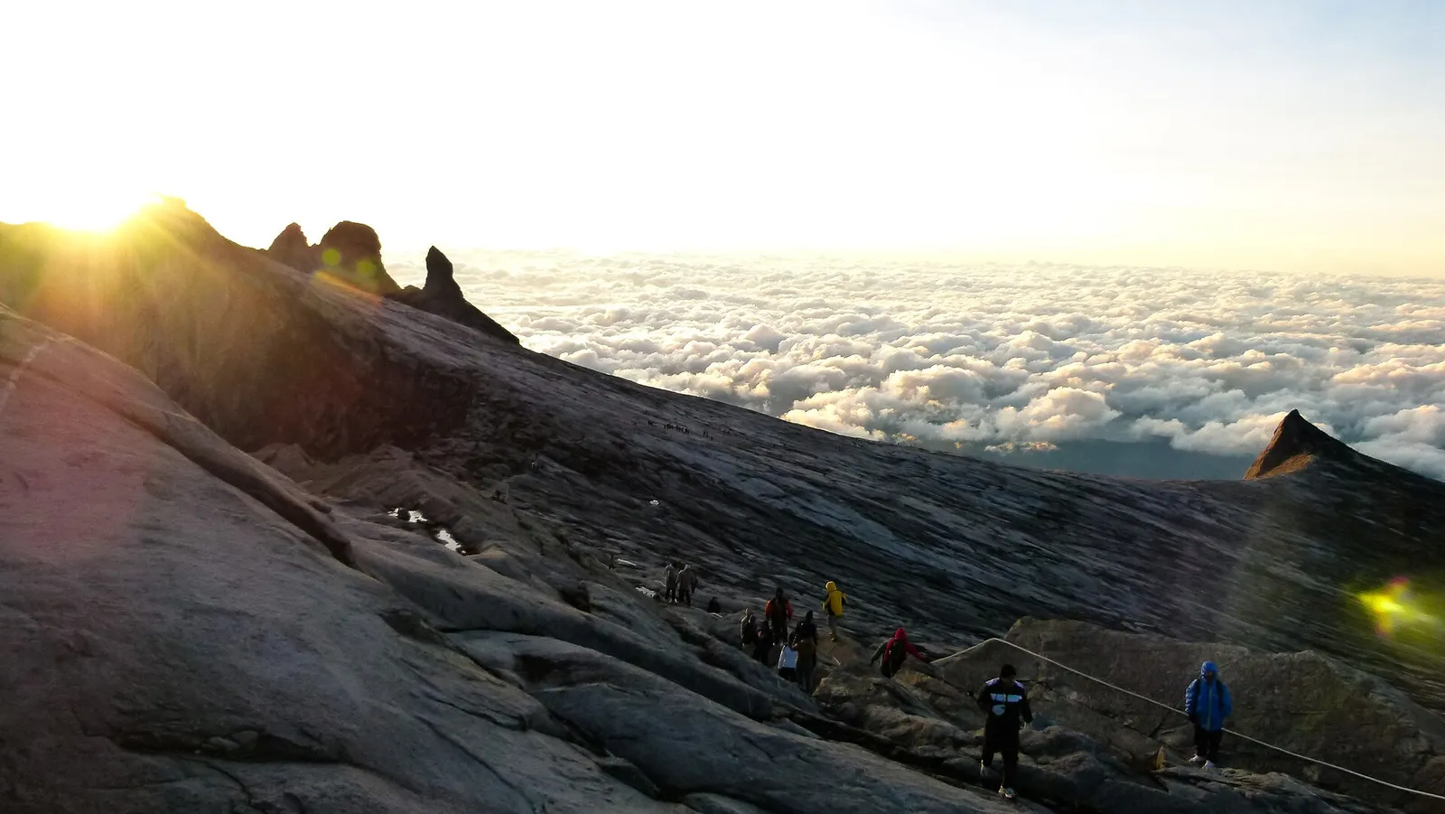 Climbers on the granite summit plateau of Mount Kinabalu at sunrise, above the clouds